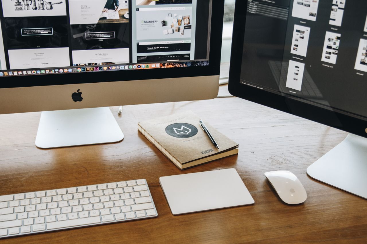Un espace de travail minimaliste avec deux moniteurs, un clavier, une souris et un carnet pour favoriser la productivité.